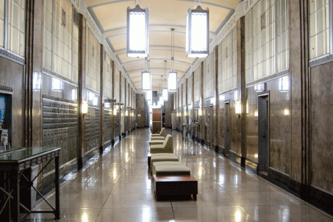 interior hallway with high ceiling with large lights suspended from the ceiling and furniture through the center of the hallway with walking space on either side of the hall. 